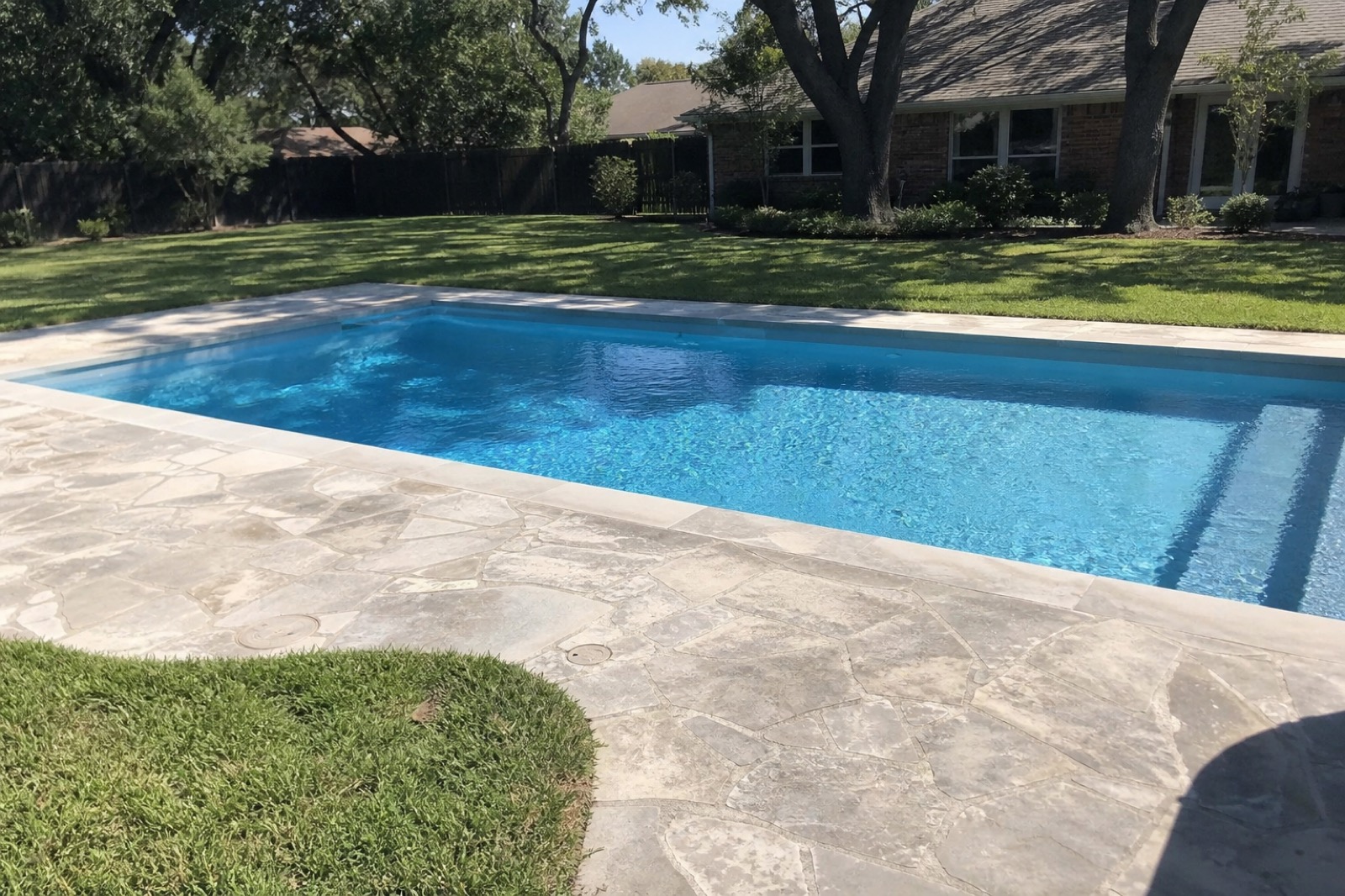 A residential pool in a Dallas backyard with flagstone deck, clear blue water, and live oaks overhead.