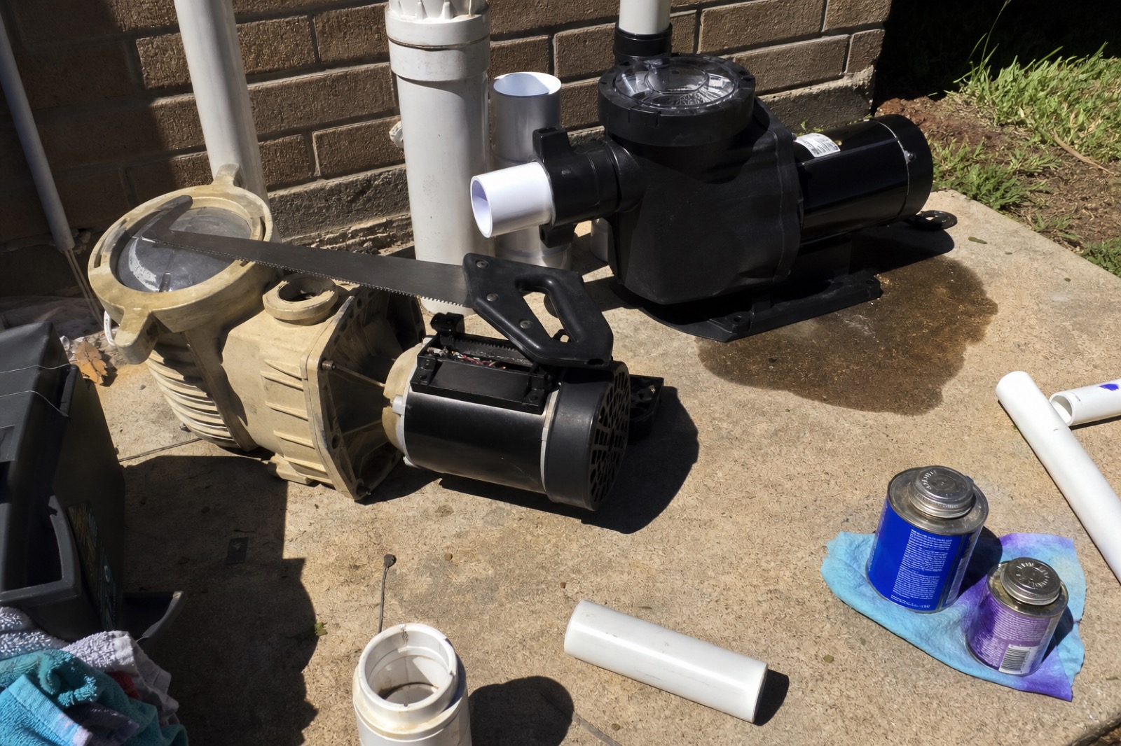 Pump replacement in progress — old beige pump pulled aside, new black pump set in place, fresh PVC cuts and primer on the equipment pad.